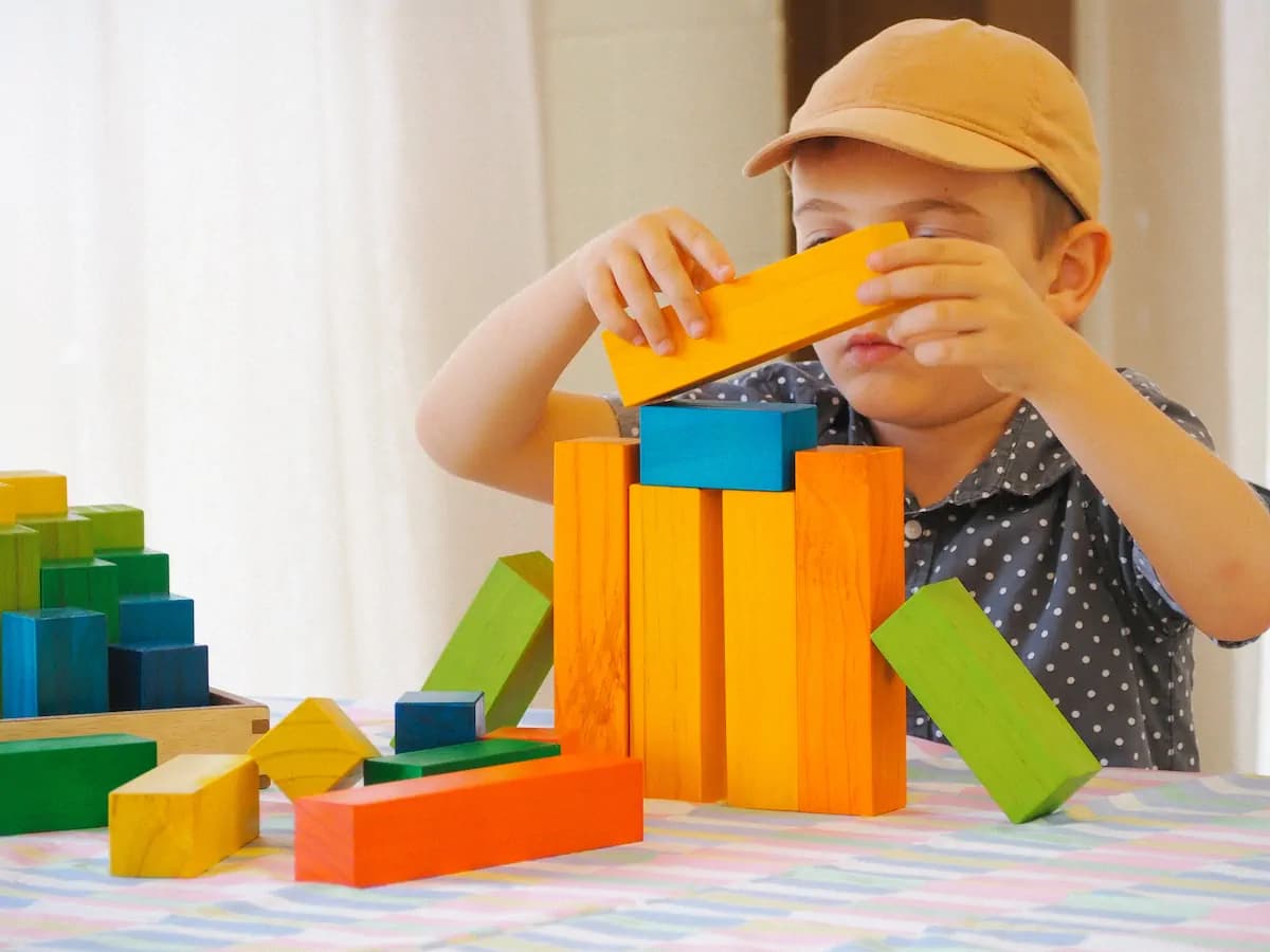 Young boy in a cap concentrating on building a tower with colourful wooden blocks